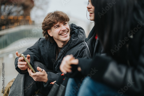 Schilderij op canvas Teenagers sit together outdoors, smiling as one shows a phone