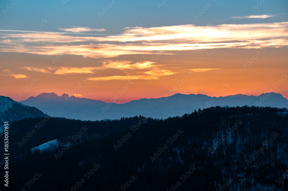 Obraz premium Colorful sunset painting mountain silhouettes and cloud layers