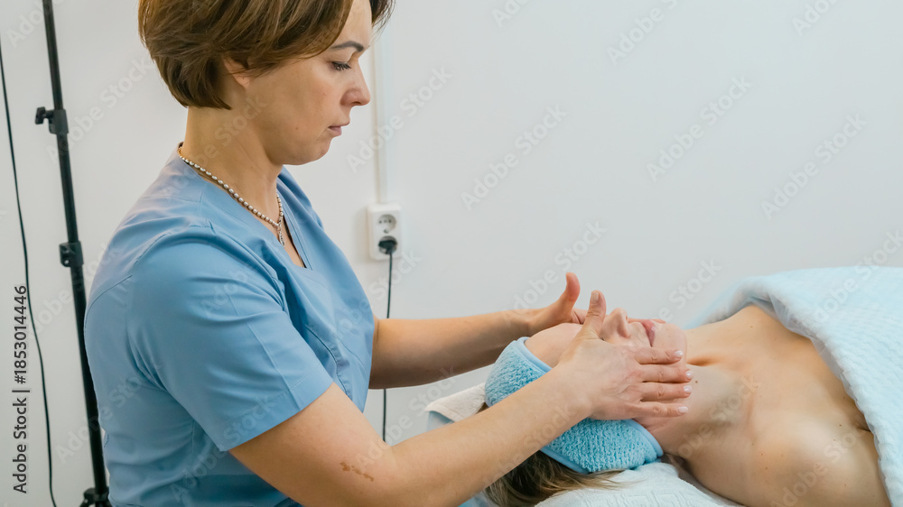 Obraz premium massage therapist performs a relaxing facial massage on a young woman lying with her eyes closed in a beauty salon or cosmetology room. professional cosmetologist performs massages for women