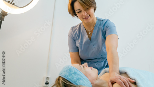 Fotografija positive professional masseuse in a cozy massage room with a female client lying