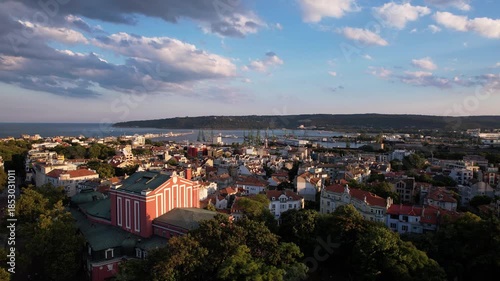Aerial view of the city with buildings, trees, and the port blending with the sea under a cloudy sky, creating a vibrant skyline, Varna, Varna, Bulgaria.