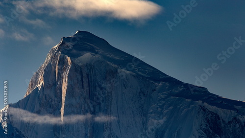 View of the majestic, snow-dusted mountain rising sharply against a clear blue sky, crowned by a single, soft cloud, Hunza, Gilgit Baltistan, Pakistan.