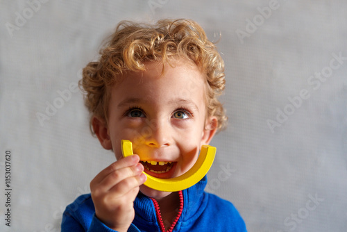 Cheerful preschool boy with curly blond hair looking up, holding a yellow building block toy creating a smile