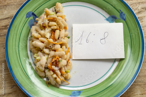  intermittent fasting concept through plate of  bean salad and a note with 16 8 written