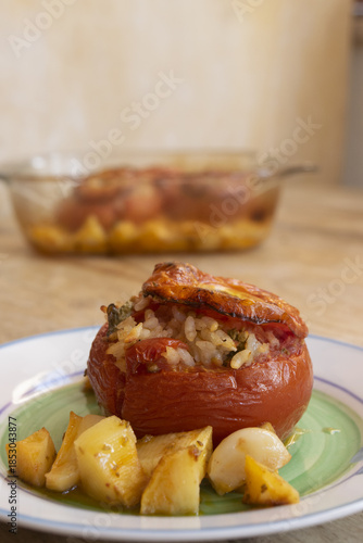 heirloom tomato stuffed with rice and herbs served with potatoes on a wooden table