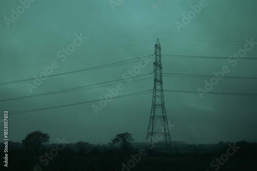 Industrial landscape with electricity pylons and transmission towers against a gloomy overcast sky. Highway with cars in the fog during a rainy day. Urban melancholy concept. England
