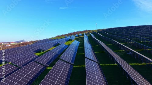 Rows of gleaming solar panels stretch across gently sloped hills, harnessing sunlight for energy in a beautiful natural setting. The scene evokes a sense of innovation and harmony.