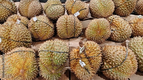 A pile of whole, thorny durian fruits displayed for sale at a local fruit stall, highlighting the texture and large size of the famous king of fruits