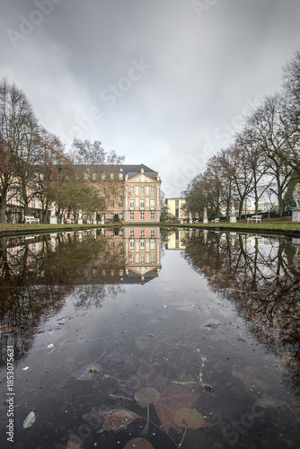 View of the Electoral Palace reflected in the still waters of the Palace Garden pond on a cloudy day, Trier, Rhineland Palatinate, Germany.