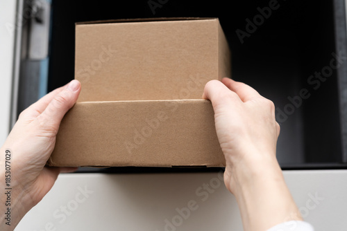 Hands place a cardboard box into a delivery drop-off location around midday in a modern area