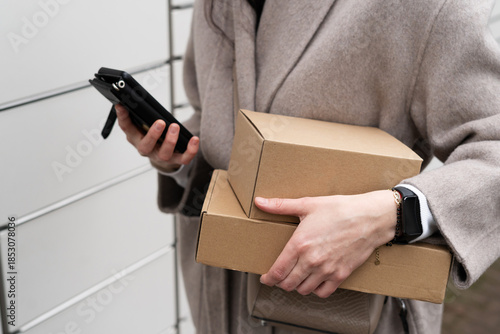 Person holding packages and a phone while standing near a delivery area in an urban setting at midday