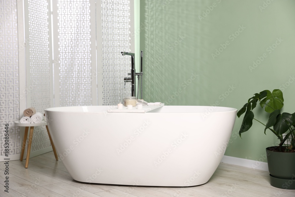 Fototapeta premium Tub, folding screen and green houseplant in bathroom. Interior design