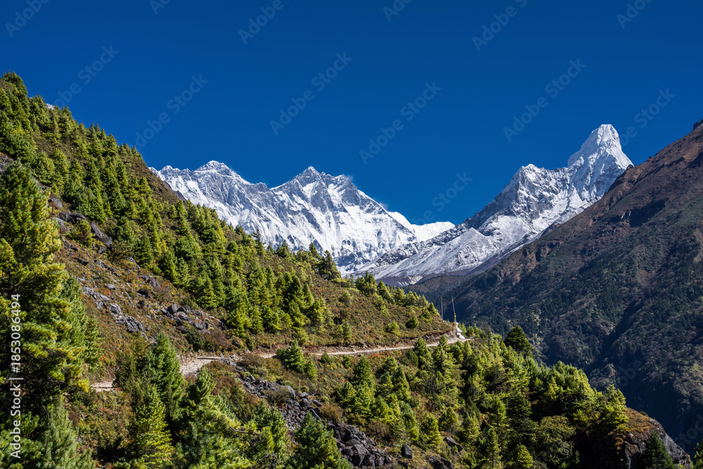 Fototapeta premium Snowy Lhotse and Ama Dablam peaks behind the mountainside and trekking route from Namche bazar to Tengboche. Everest base camp trek in Nepal.
