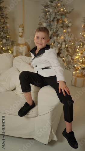 Stylish young boy in formal suit sitting confidently on sofa in festive Christmas interior