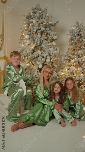 Mother and children in matching green pajamas posing together by decorated Christmas trees indoors