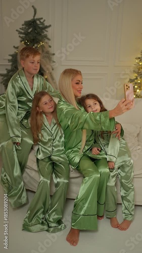 Happy mother and children wearing matching green pajamas taking selfie in cozy Christmas living room