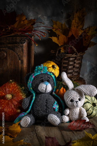 Knitted toys. A bear and a hare on a wooden table surrounded by autumn leaves and pumpkins.
