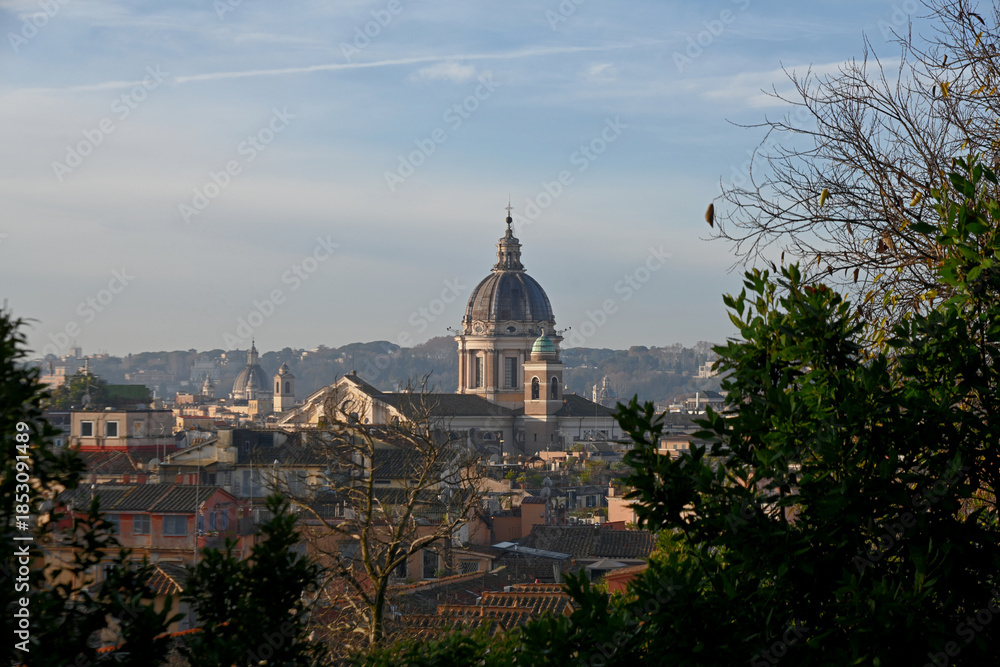 Fototapeta premium Elevated view across the rooftops of Rome, Italy, featuring the domes of historic churches illuminated by warm evening light. The timeless skyline showcases the Eternal City's remarkable blend of Rena
