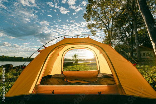 A cozy yellow camping tent pitched on lush green grass by a peaceful lakeside during golden hour. nature travel, and serene outdoor living. Ideal for themes of camping, weekend getaway,