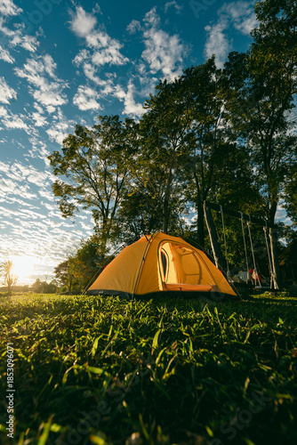 A cozy yellow camping tent pitched on lush green grass by a peaceful lakeside during golden hour. nature travel, and serene outdoor living. Ideal for themes of camping, weekend getaway,