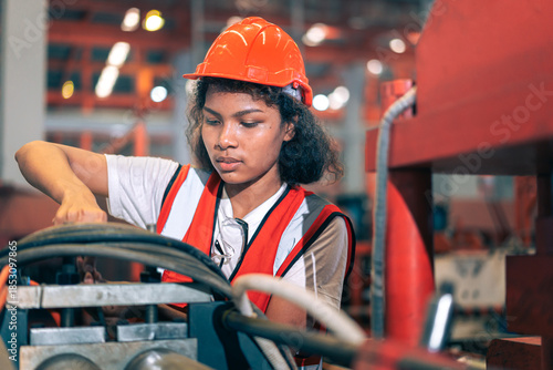 Professional Black African female factory engineer/worker/technician operate machinery in modern industrial plant. She wear safety helmet,vest show focus,skill in repair maintenance production process