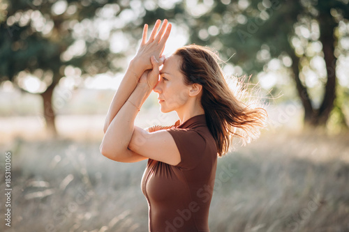 A woman practices a calm stretching pose outdoors, surrounded by trees and soft natural light, creating a peaceful and balanced atmosphere.