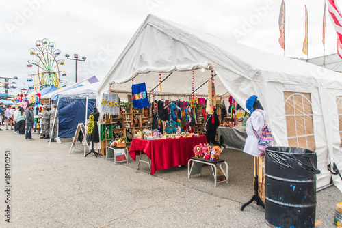 A bustling street fair lined with vendor booths, with a Ferris wheel towering in the distance, Cumming, Georgia, United States of America