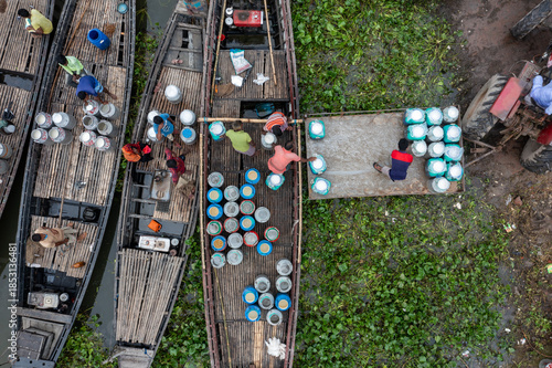 Sirajganj, Bangladesh - 12 July 2020: Aerial view of boats laden with containers, a symphony of blues and browns against the lush greenery, showcasing a vibrant riverine trade..