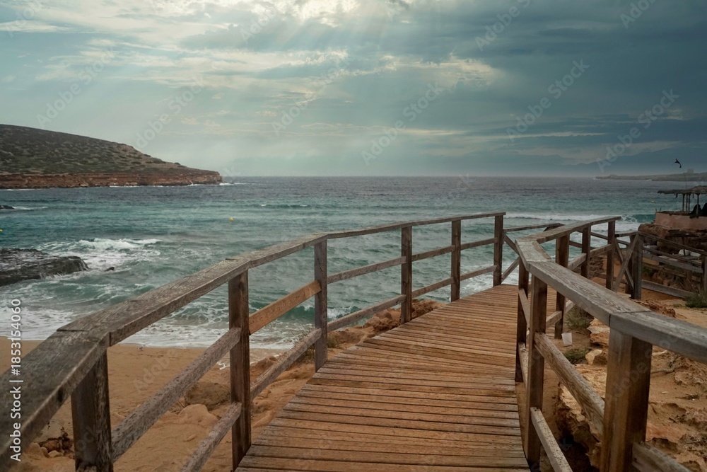 Fototapeta premium panorama con molo di legno per accesso alla spiaggia con sfondo di mare mosso e cielo nuvoloso con temporale in arrivo