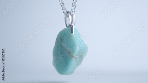 Close up of a blue gemstone pendant on a silver chain against a clean background