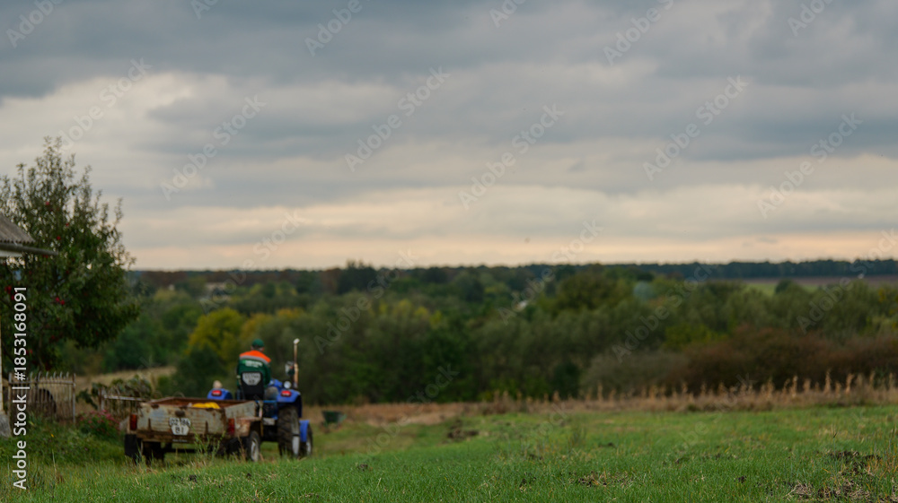 Fototapeta premium Farmer driving a tractor with a trailer through a field on a cloudy day