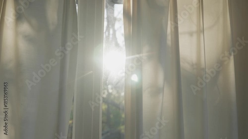 Sunlight shining inside home or apartment through glass window with curtain. Daylight entering room. Bright summer day with forest or natural background. Early morning or afternoon light lens flare