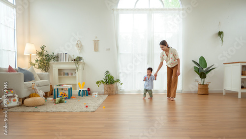 Boy Takes His First Steps at Home While Holding His Mother's Hand in a Warm Living Room Setting
