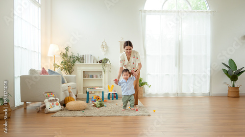 Boy Takes His First Steps at Home While Holding His Mother's Hand in a Warm Living Room Setting