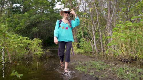 A mature woman enjoys a hike in Charco Verde park on Ometepe Island, stepping through water and observing the surroundings in Nicaragua.