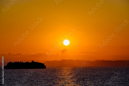 Silhouette of a cruise ship at sea during an orange sunset sky over the horizon	