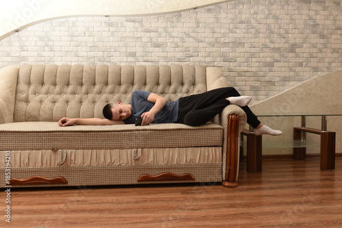 Young man lying on sofa at home using smartphone, relaxing indoors in casual clothes with calm mood and comfortable domestic interior