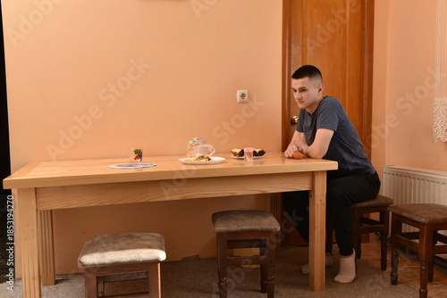 Young man sitting alone at kitchen table with food, thoughtful mood at home, everyday domestic scene, simple lifestyle and quiet moment indoors