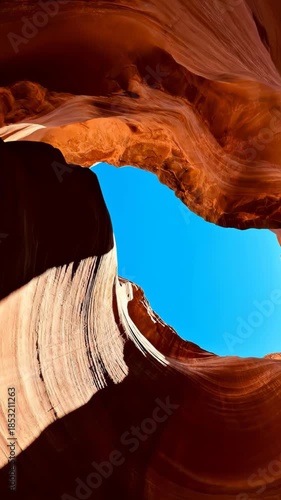 Low angle view of smooth orange sandstone walls in a slot canyon against a bright blue sky