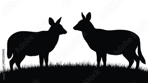 Two black silhouettes of goats standing on grass facing each other