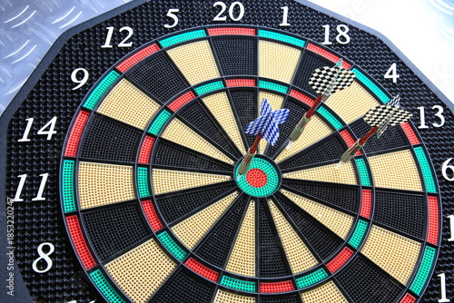 Drei Dartpfeile stecken präzise in der Dartscheibe. Die kräftigen Farben und der metallische Hintergrund betonen den Moment sportlicher Konzentration.