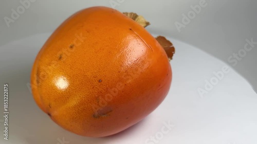 A close-up shot of a single, round, vibrant orange persimmon fruit with a smooth, slightly textured peel, slowly spinning on a clean white background, ideal for food, health, and market themes.