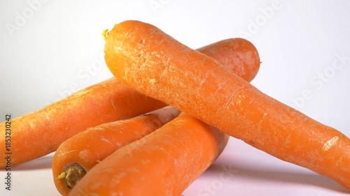 A close-up shot of several bright orange, cylindrical carrots piled and slowly spinning against a clean white background, emphasizing their fresh, natural, and healthy appearance.