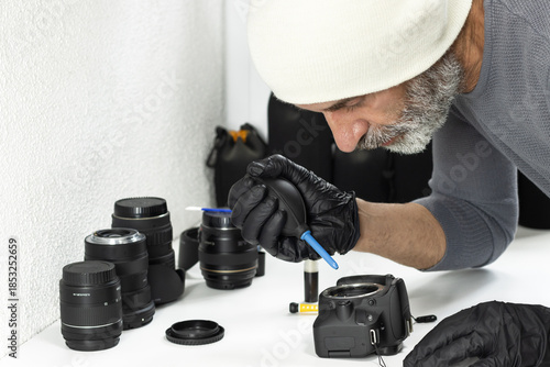 Technician wearing gloves cleaning a DSLR camera sensor with air blower. Camera maintenance, photography equipment care, studio workspace, precision and technology.