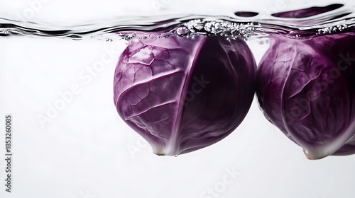 Two vibrant red cabbages momentarily submerged in clear water, their textures enhanced by the water's rippling surface, set against a crisp white backdrop. A striking visual.
