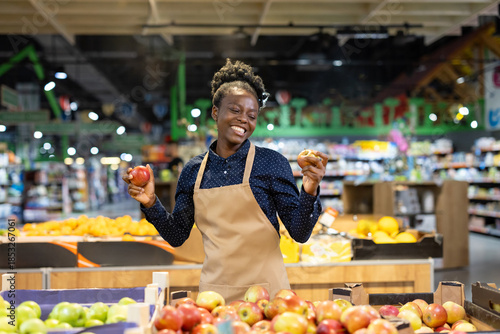 Foto Happy african american grocery worker wearing an apron, smiling while holding fr