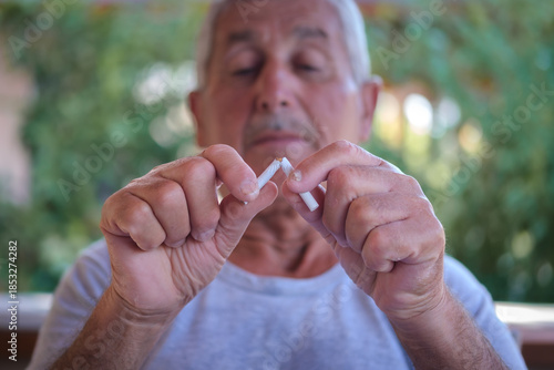 Senior man breaking a cigarette to quit smoking and choose a healthy lifestyle.