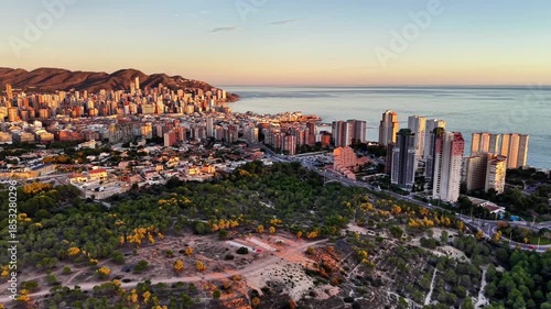 aerial parkland and urban skyline at dawn soft light on buildings green foreground leading to beachfront