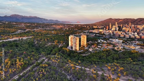 aerial view twin towers rising from forest edge with city skyline beyond and golden light, marketing team