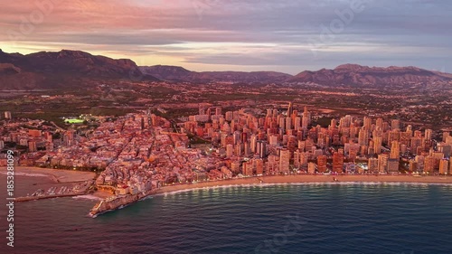 aerial view coastal city at sunset with illuminated beachfront and mountain backdrop, tourism board captures